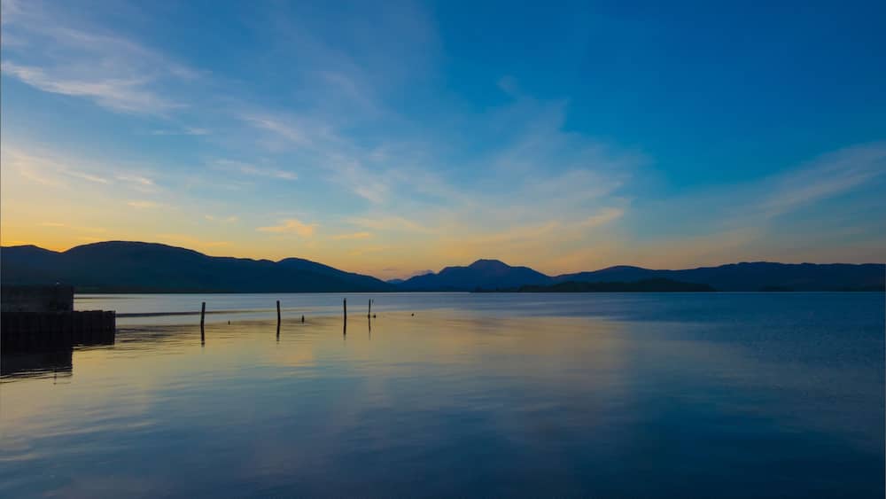 Un lac paisible au coucher du soleil, avec des montagnes en arrière-plan.