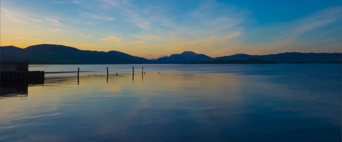 A calm lake at sunset with mountains in the background.