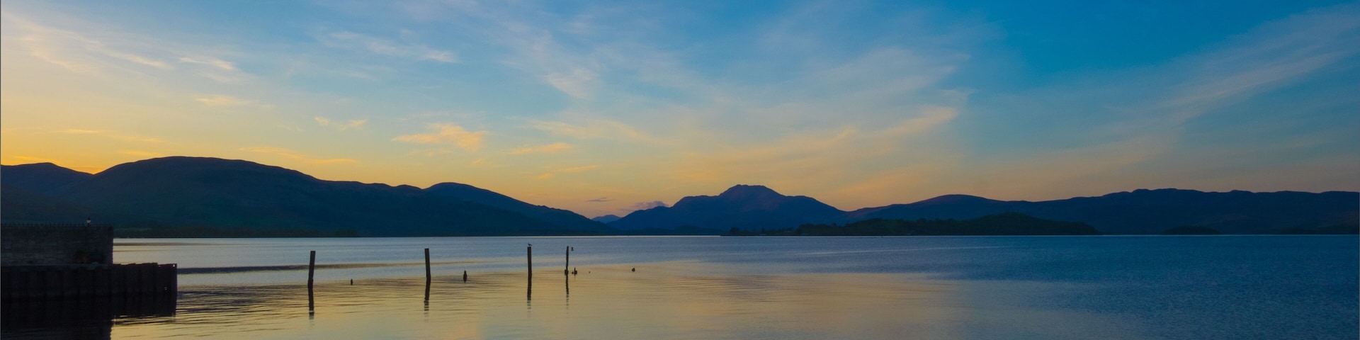 A calm lake at sunset with mountains in the background.