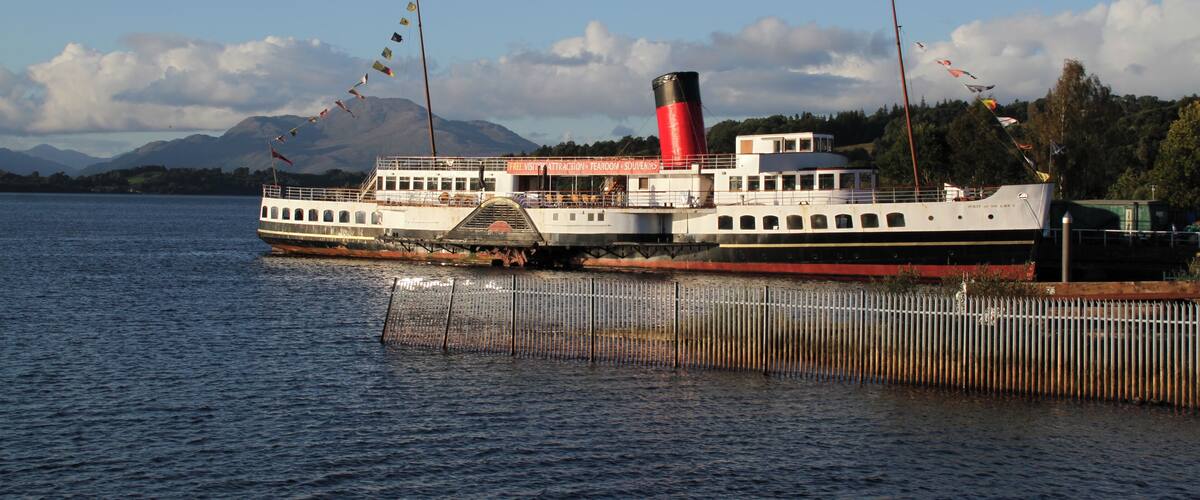 A steamboat docked at a pier with mountains in the background.