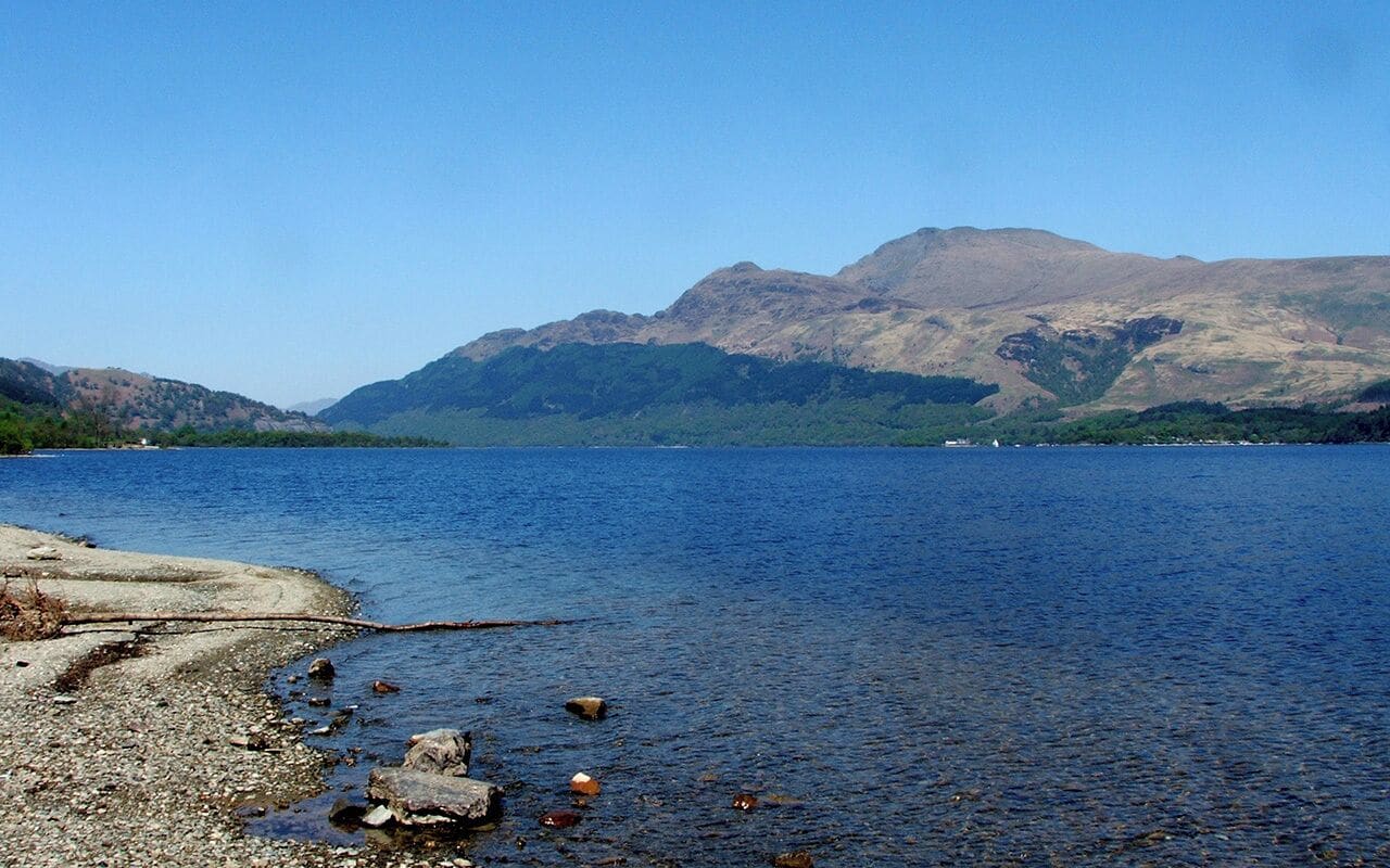 A calm lake with rocky shores and mountains in the background.