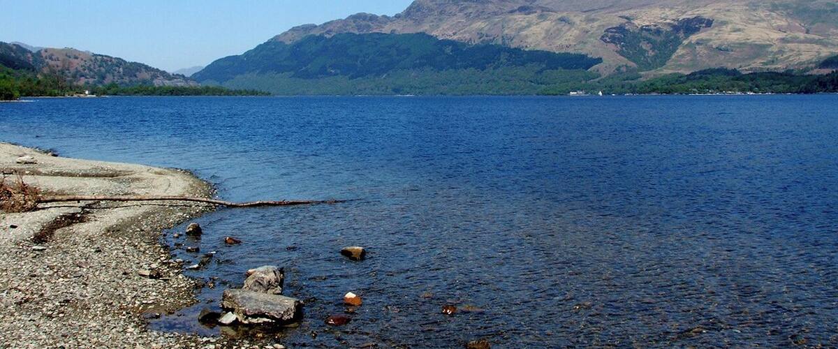 A calm lake with rocky shores and mountains in the background.