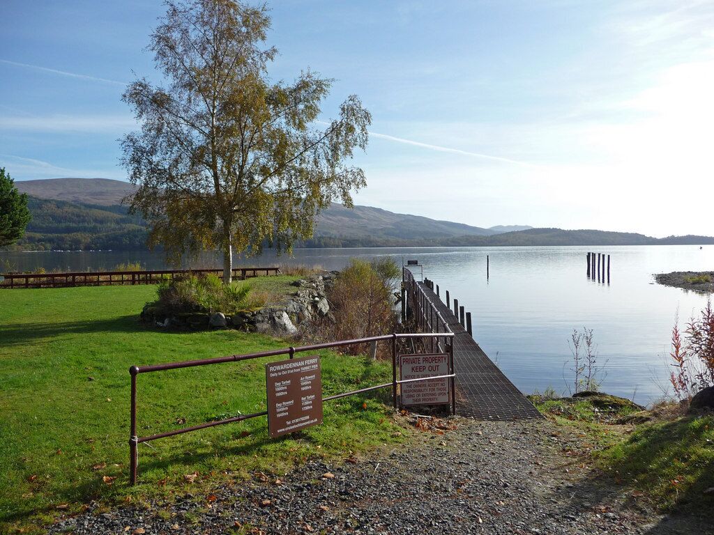 A serene lake with a wooden dock, a sign indicating private property, and a grassy area with a tree.