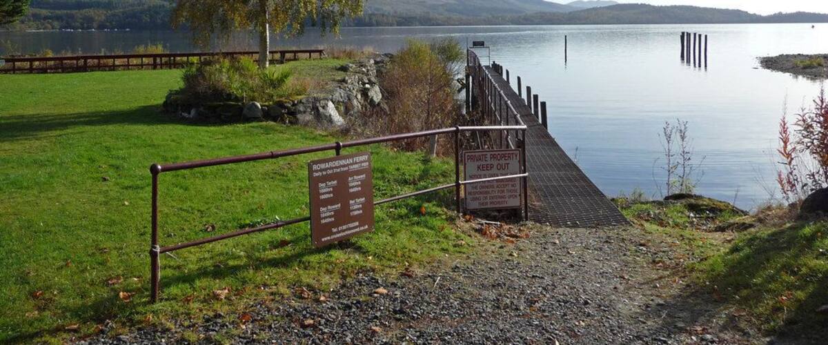 A serene lake with a wooden dock, a sign indicating private property, and a grassy area with a tree.