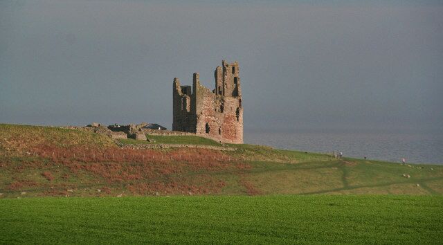 A historic stone castle on a grassy hill overlooking the sea.