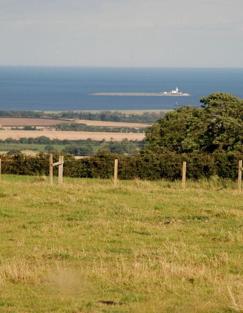 Fields below Hillhead This mixed agricultural land slopes down to the sea. Coquet Island can be seen in the background about 10 kilometres away.