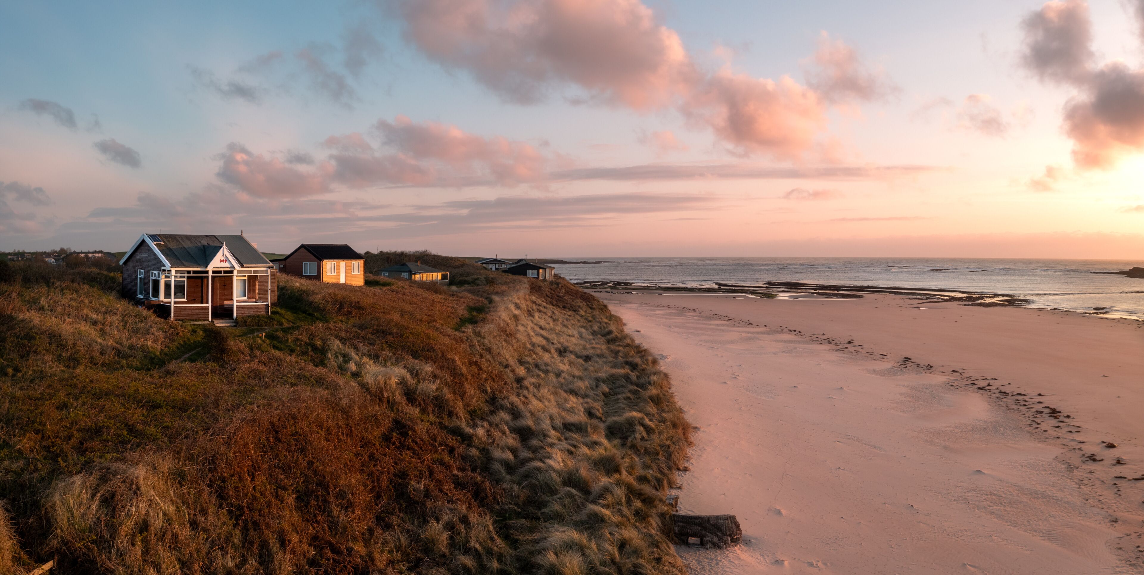 A beach with dunes, a wooden structure, and a house with a metal roof.