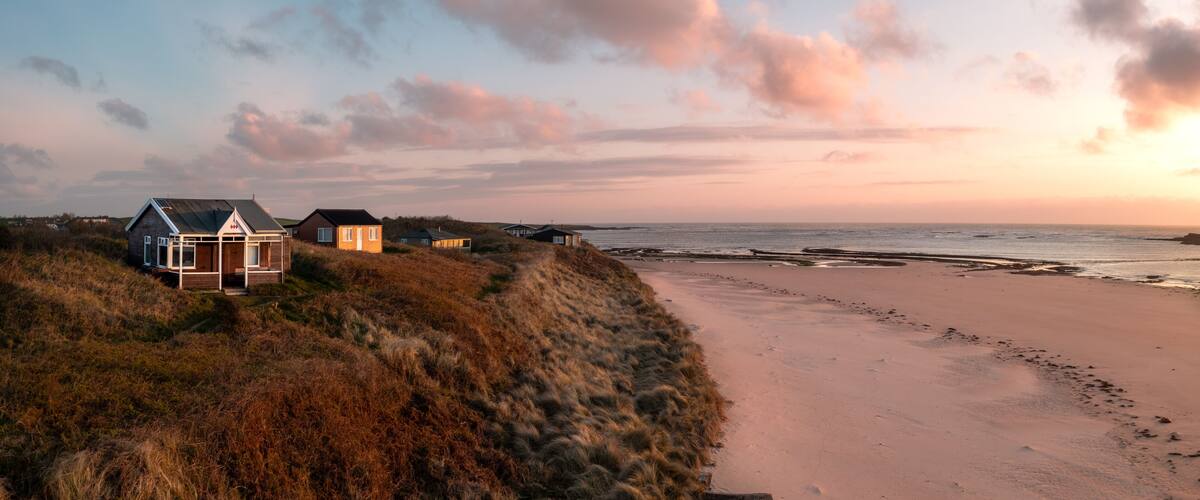 A beach with dunes, a wooden structure, and a house with a metal roof.