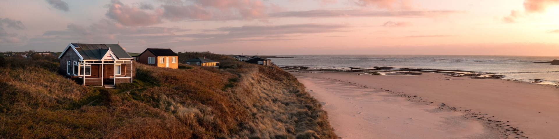 A beach with dunes, a wooden structure, and a house with a metal roof.