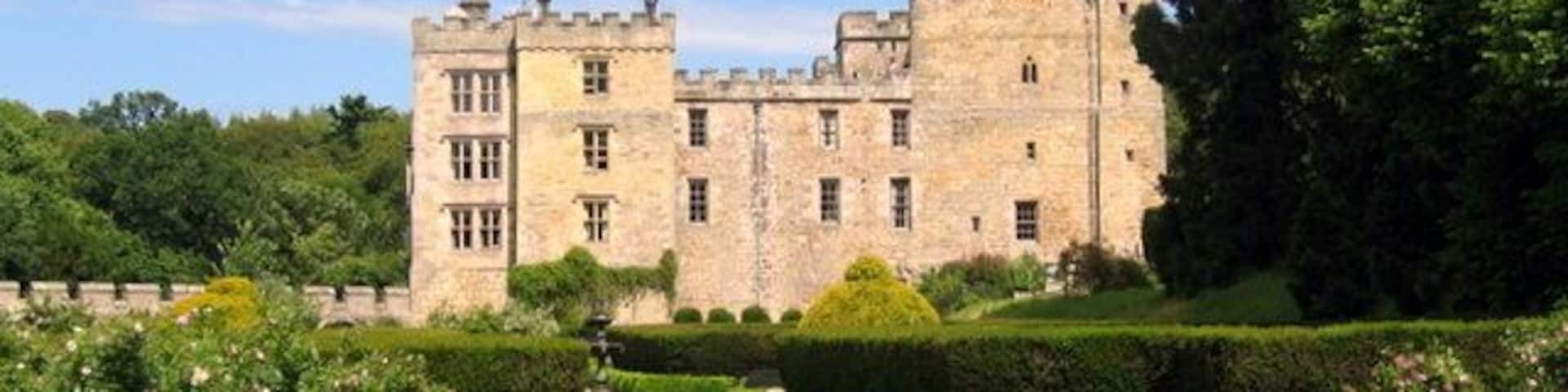 A historic stone castle with a formal garden and a clear sky.