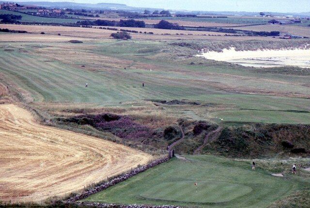 A golf course with rolling green hills and a sandy area.