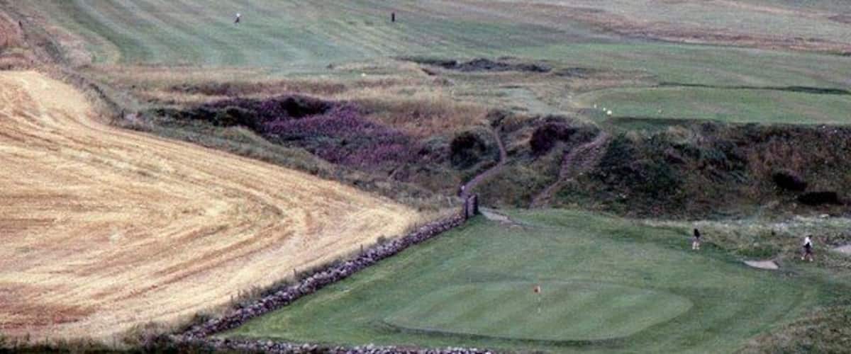 A golf course with rolling green hills and a sandy area.