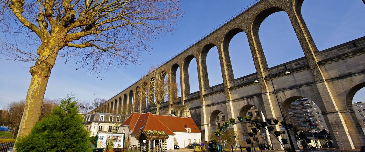 A large stone bridge with multiple arches, a tree with bare branches, and a building with a red roof in the foreground.