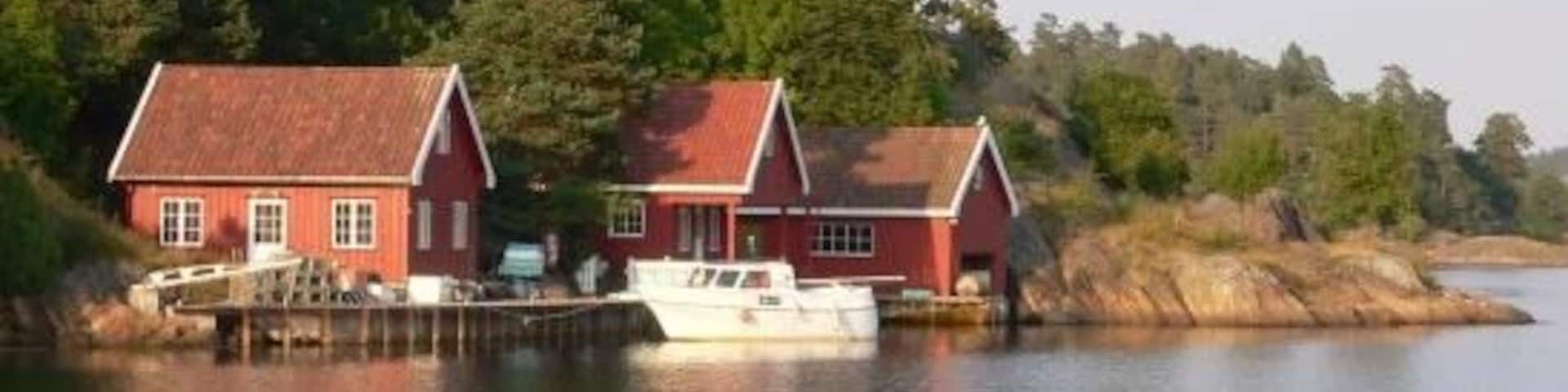 Two red houses by a calm lake with a boat docked in front.