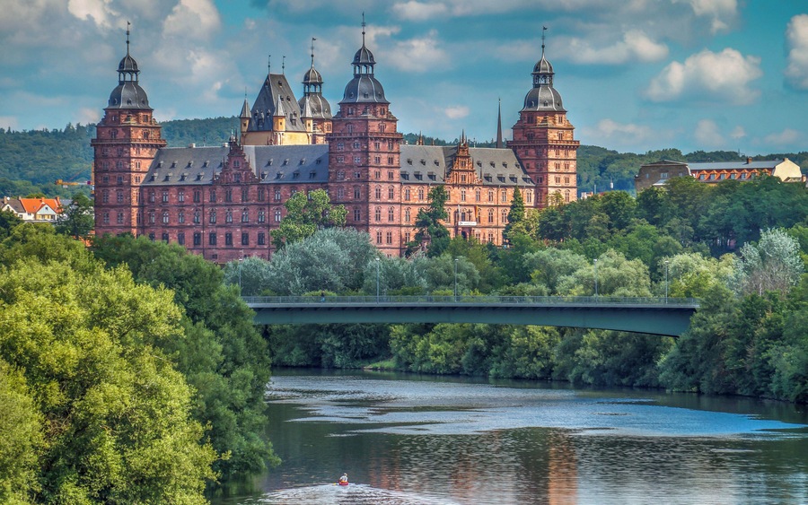 Ein historisches Gebäude aus rotem Backstein mit mehreren Türmen, einem Fluss und einer Brücke.