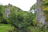 A lush green valley with a river, rocky cliffs, and a dirt path.