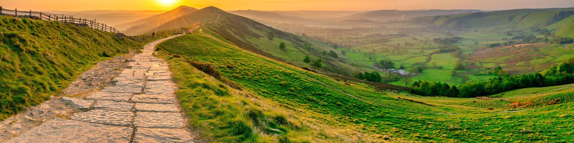 A stone pathway winding through a green hillside with a sunset in the background.