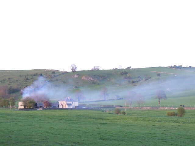 A rural landscape with a house, green fields, and smoke rising from a chimney.