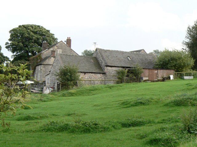 A stone house with a sloped roof, surrounded by a grassy field and trees.