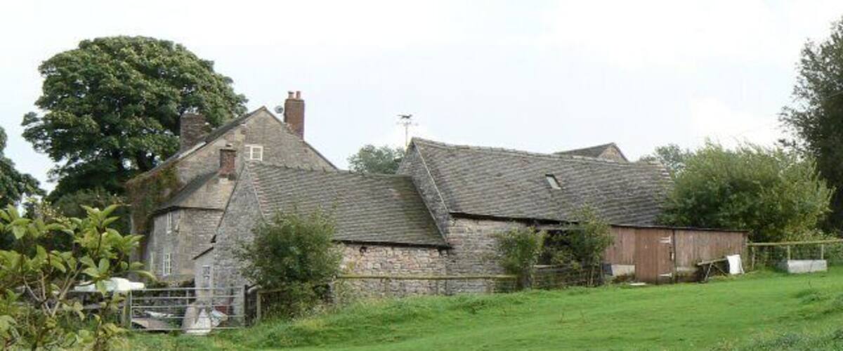 A stone house with a sloped roof, surrounded by a grassy field and trees.