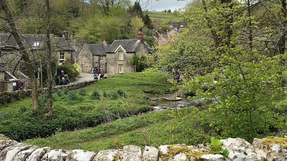 A stone wall, a stone building, and a grassy area with trees.