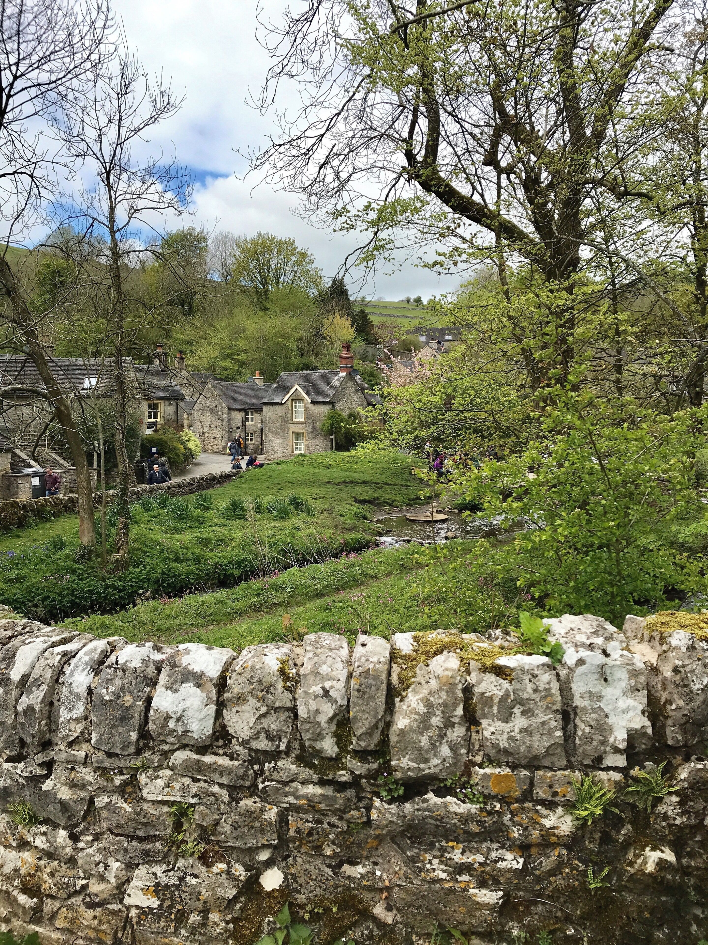 A stone wall, a stone building, and a grassy area with trees.