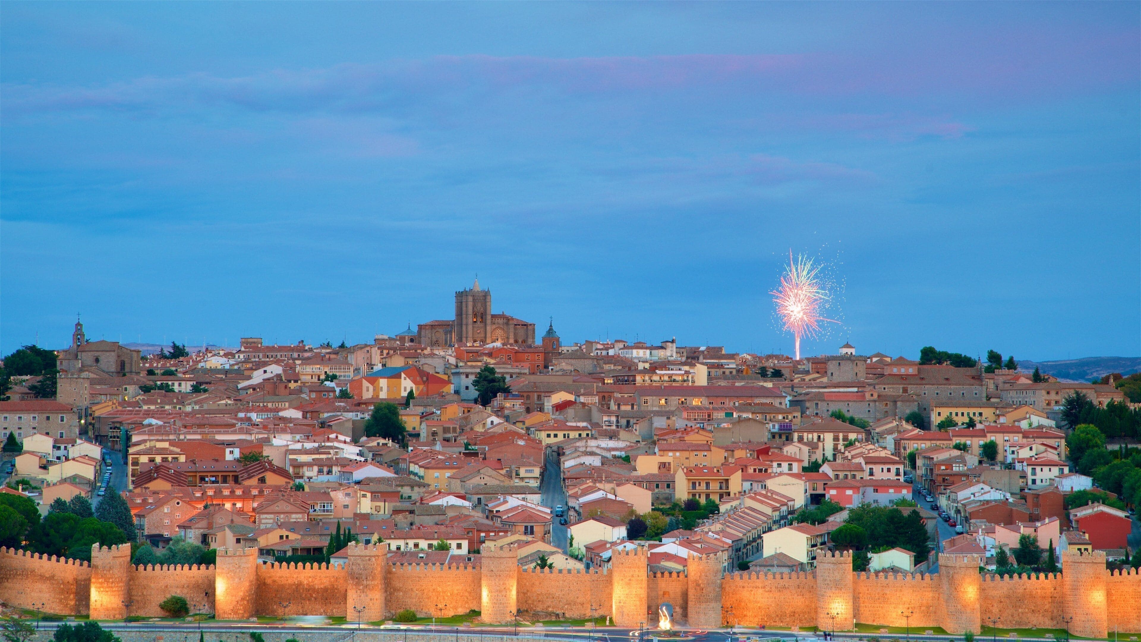 A historic cityscape with a prominent cathedral, a castle wall, and fireworks in the sky.