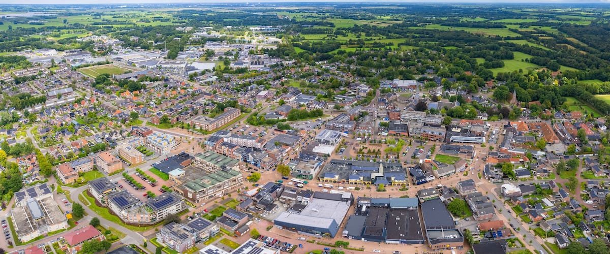 An aerial view of a town with a mix of residential and commercial buildings, surrounded by green fields and forests.