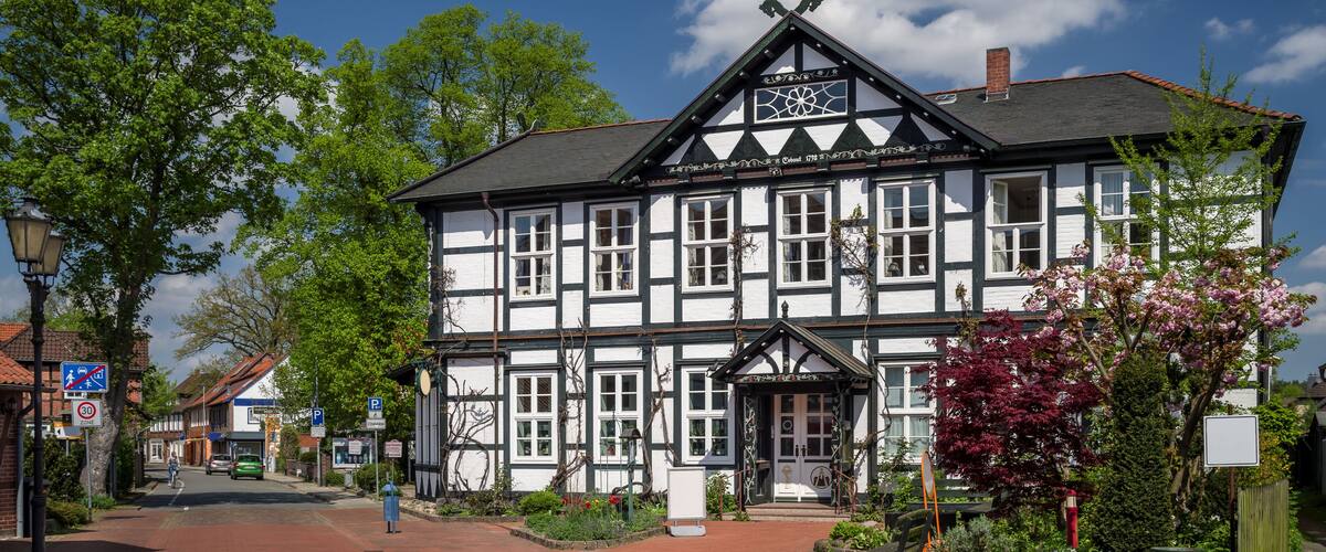 A traditional half-timbered building with a clock tower, surrounded by trees and a paved street.