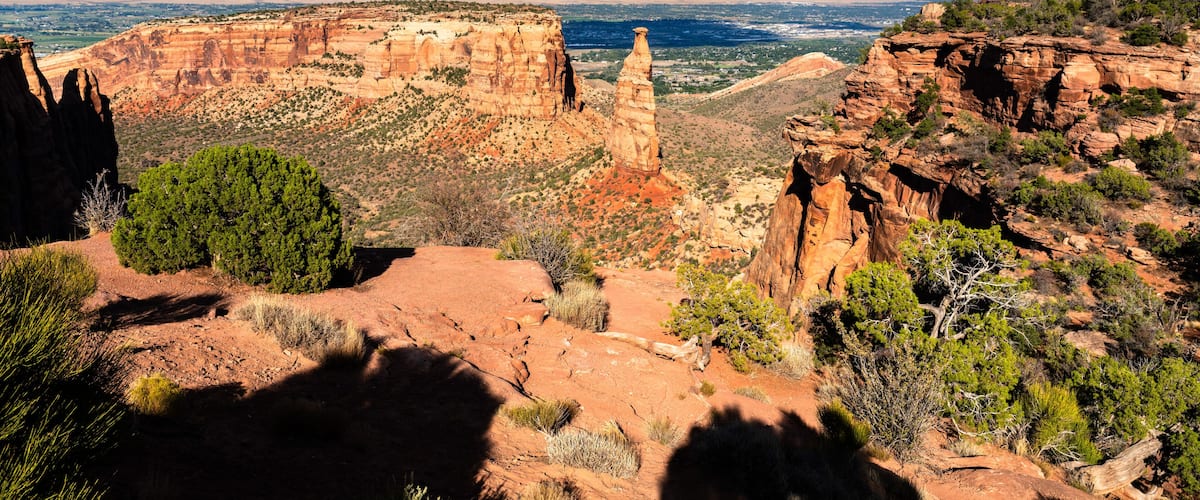 View of the iconic Independence Monument spire in Colorado National Monument. The Grand Valley and Book Cliffs are visible in the background