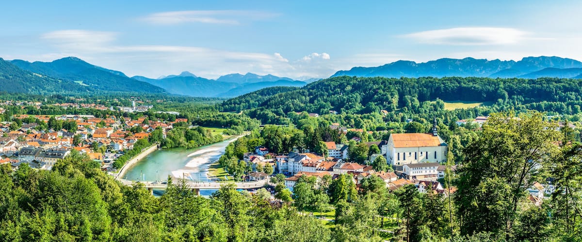 A town nestled by a river, surrounded by mountains and dense forests.