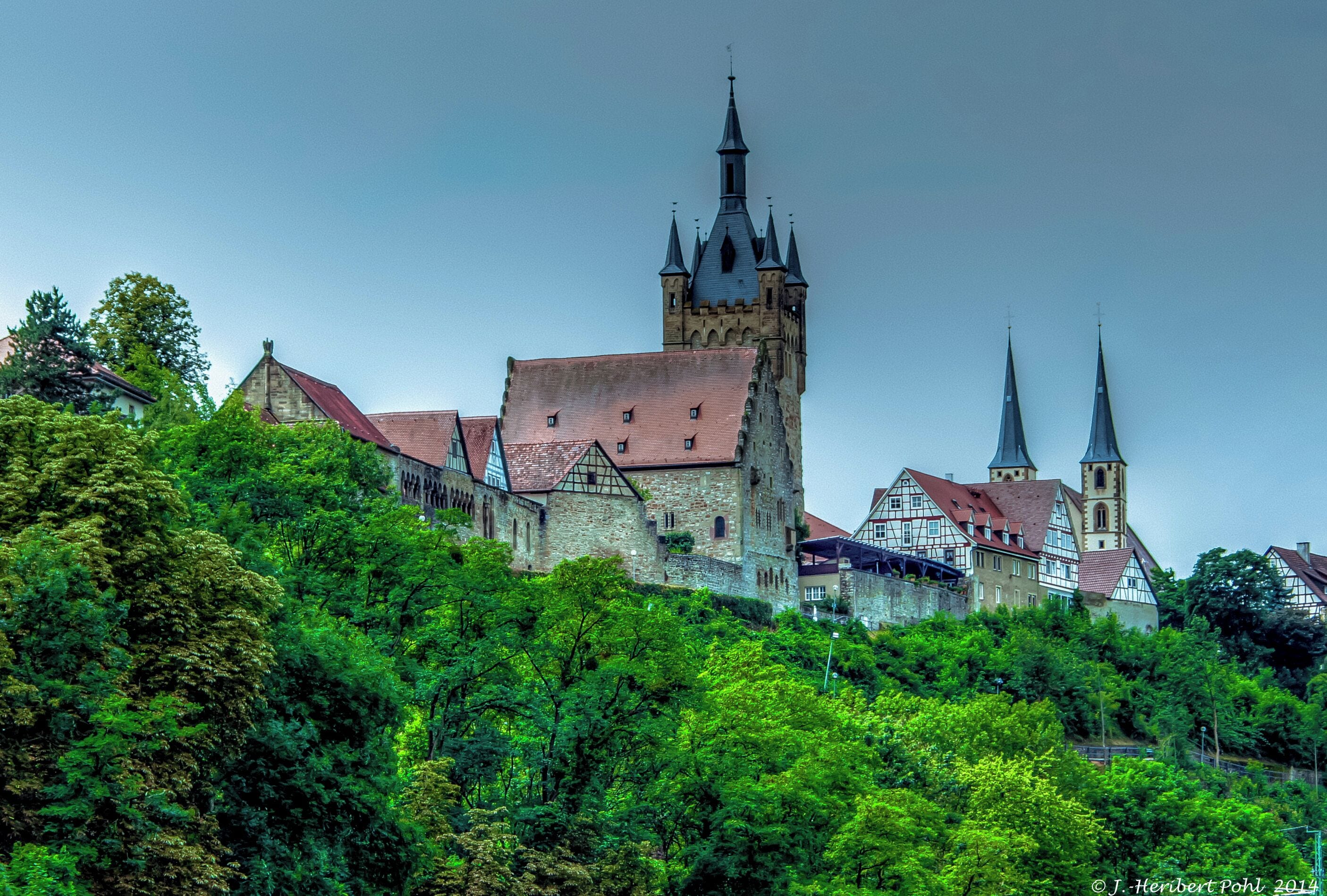 A historic castle with a prominent tower and spires, surrounded by lush greenery.