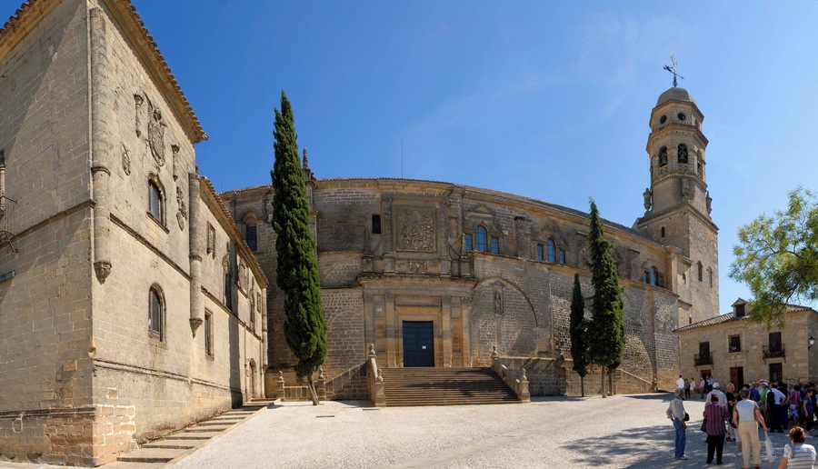A historic building with a central courtyard, tall cypress trees, and a bell tower.
