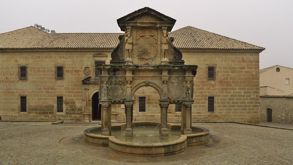 Un bâtiment historique en pierre, doté d’une cour, d’une fontaine et d’un toit recouvert de tuiles.