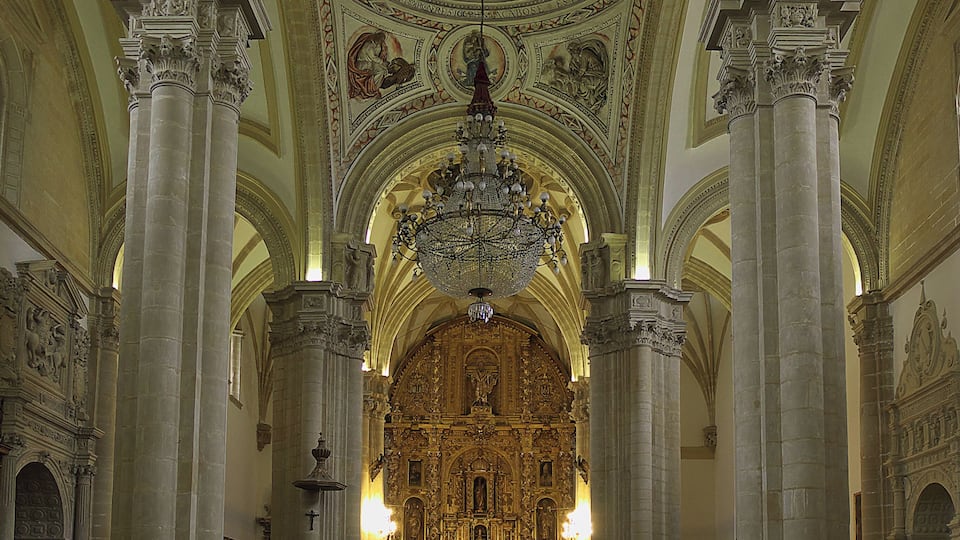 L’intérieur d’une église richement décorée, avec de hauts plafonds, des fresques détaillées et un autel central.