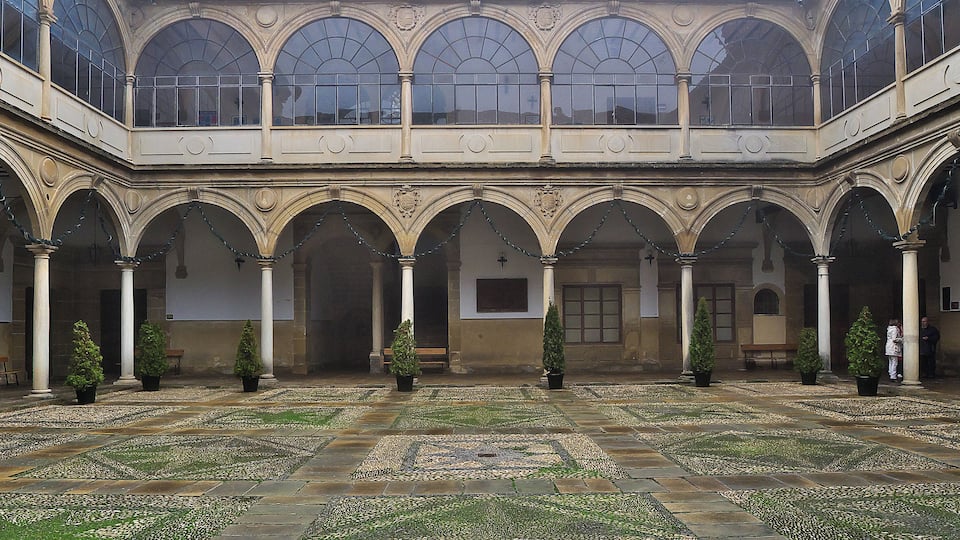 Une cour avec un sol carrelé, des arcades et des plantes en pot.