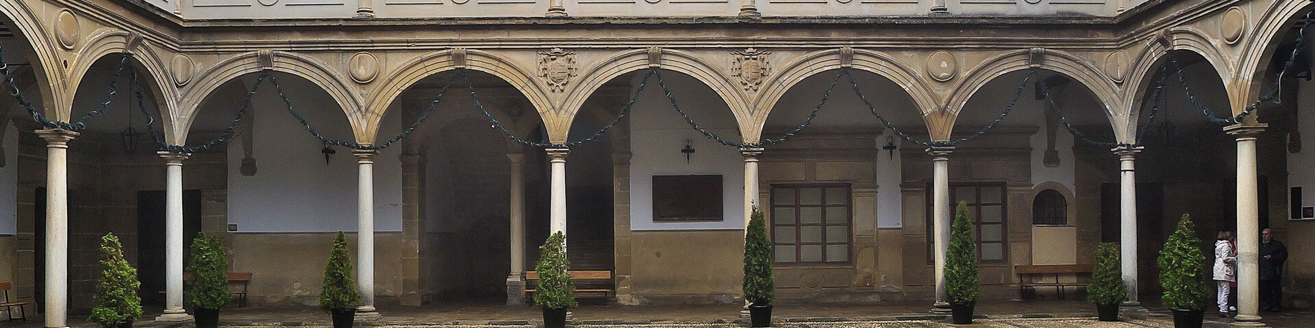 Un patio con suelo de baldosas, arcos y plantas en macetas.
