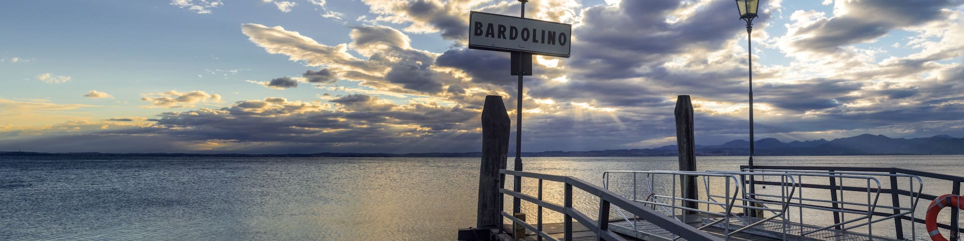 Sunset over pier at lake Garda in Bardolino Italy. Panoramic view on sunset over pier and beautiful lake Garda (Lago di Garda), mountaines in Bardolino harbour (Verona, Lombrady, Italy).