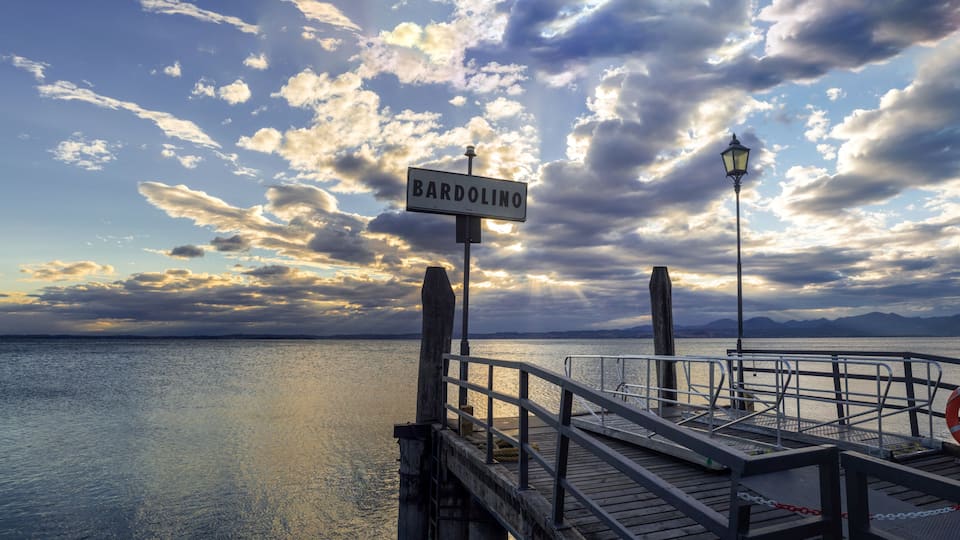 A pier with a sign reading 'BARDOLINO,' a lifebuoy, and a cloudy sky over water.