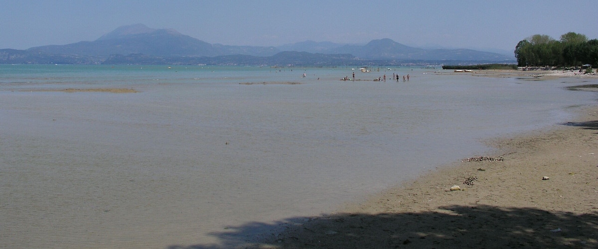 A wide sandy beach with calm waters, distant mountains, and a few people in the distance.