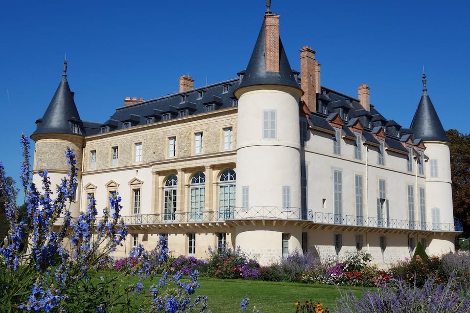 A large, historic building with multiple towers and a well-maintained garden with various flowers.