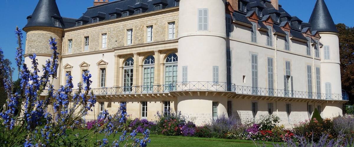 A large, historic building with multiple towers and a well-maintained garden with various flowers.