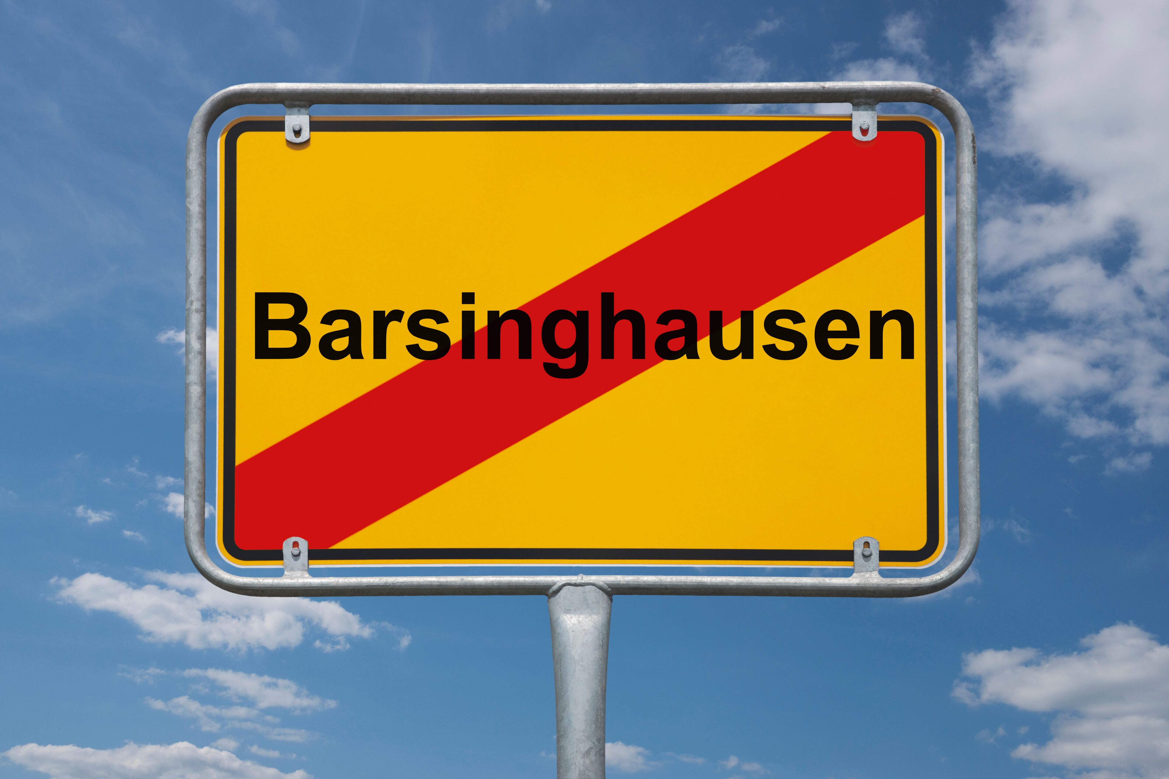 A yellow sign with red diagonal stripes and the text "Barsinghausen" against a blue sky with clouds.