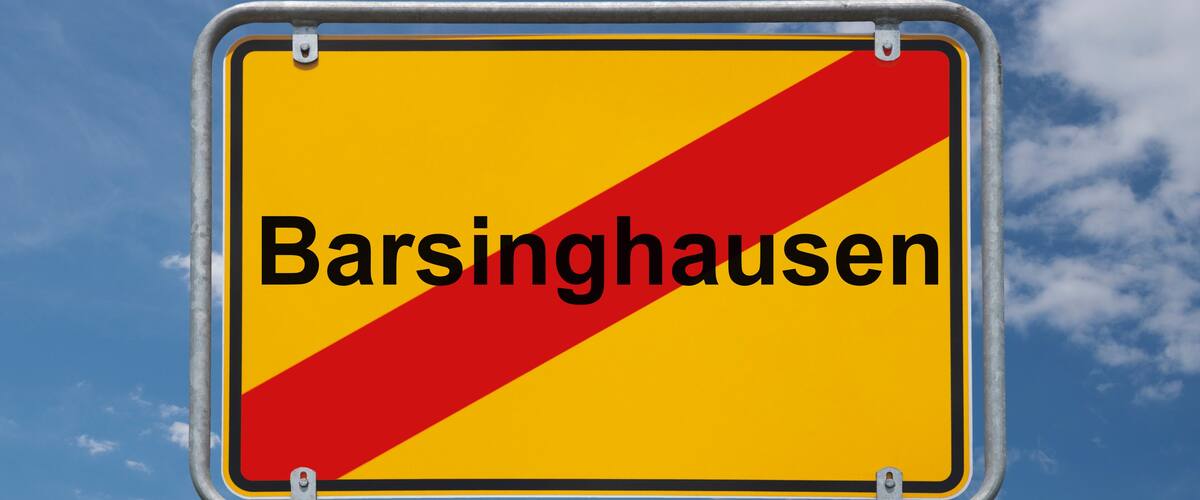 A yellow sign with red diagonal stripes and the text "Barsinghausen" against a blue sky with clouds.