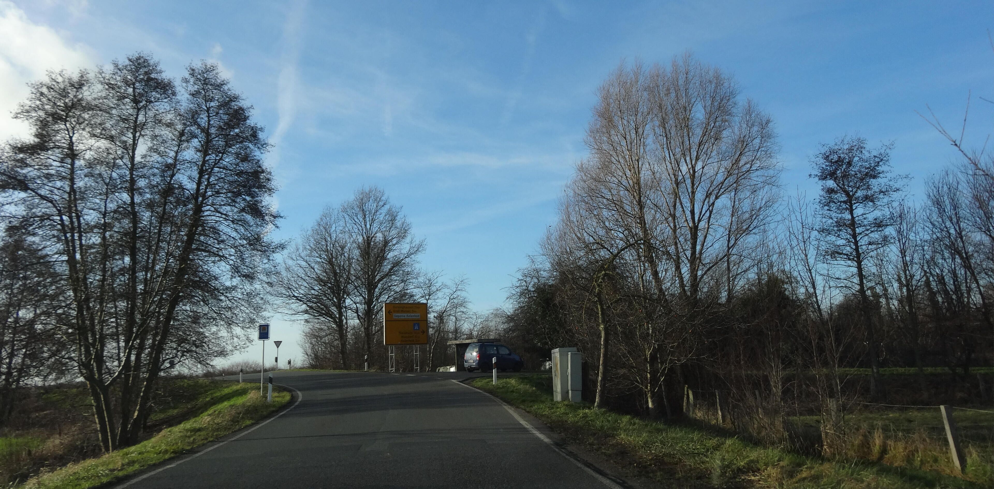 Barsinghausen, Germany. Blick von der Ortszufahrt von Holtensen in Richtung Landesstraße, mit Richtungstafel und ehemaliger Bushaltestelle.