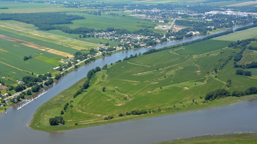 A river winding through a green valley with a small town and marina along its banks.
