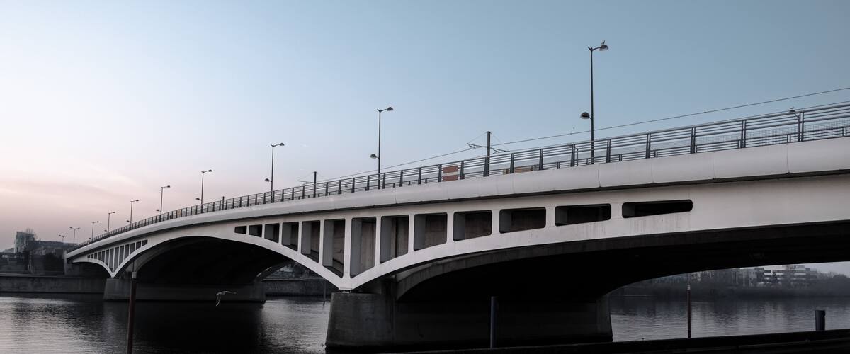 A white bridge with multiple arches over a body of water, with street lamps and a clear sky in the background.