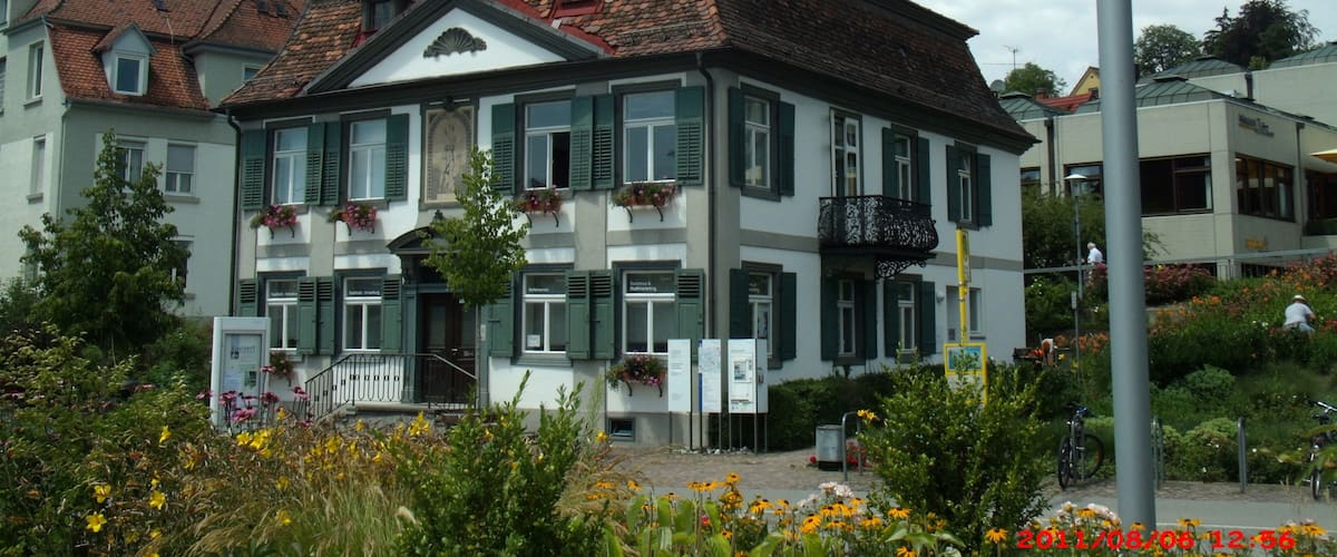 A historic building with green shutters and flower boxes, surrounded by a garden with various flowers.
