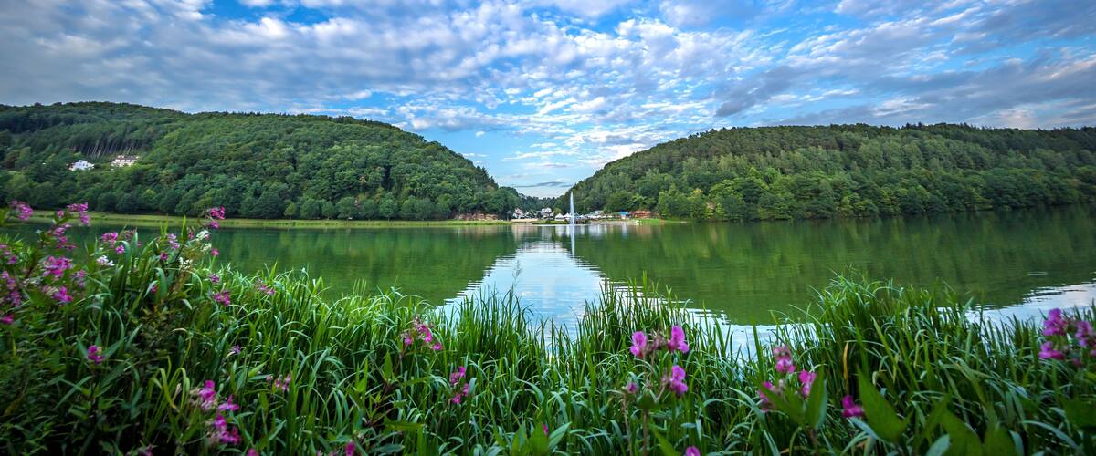 A calm lake surrounded by lush green hills under a partly cloudy sky.