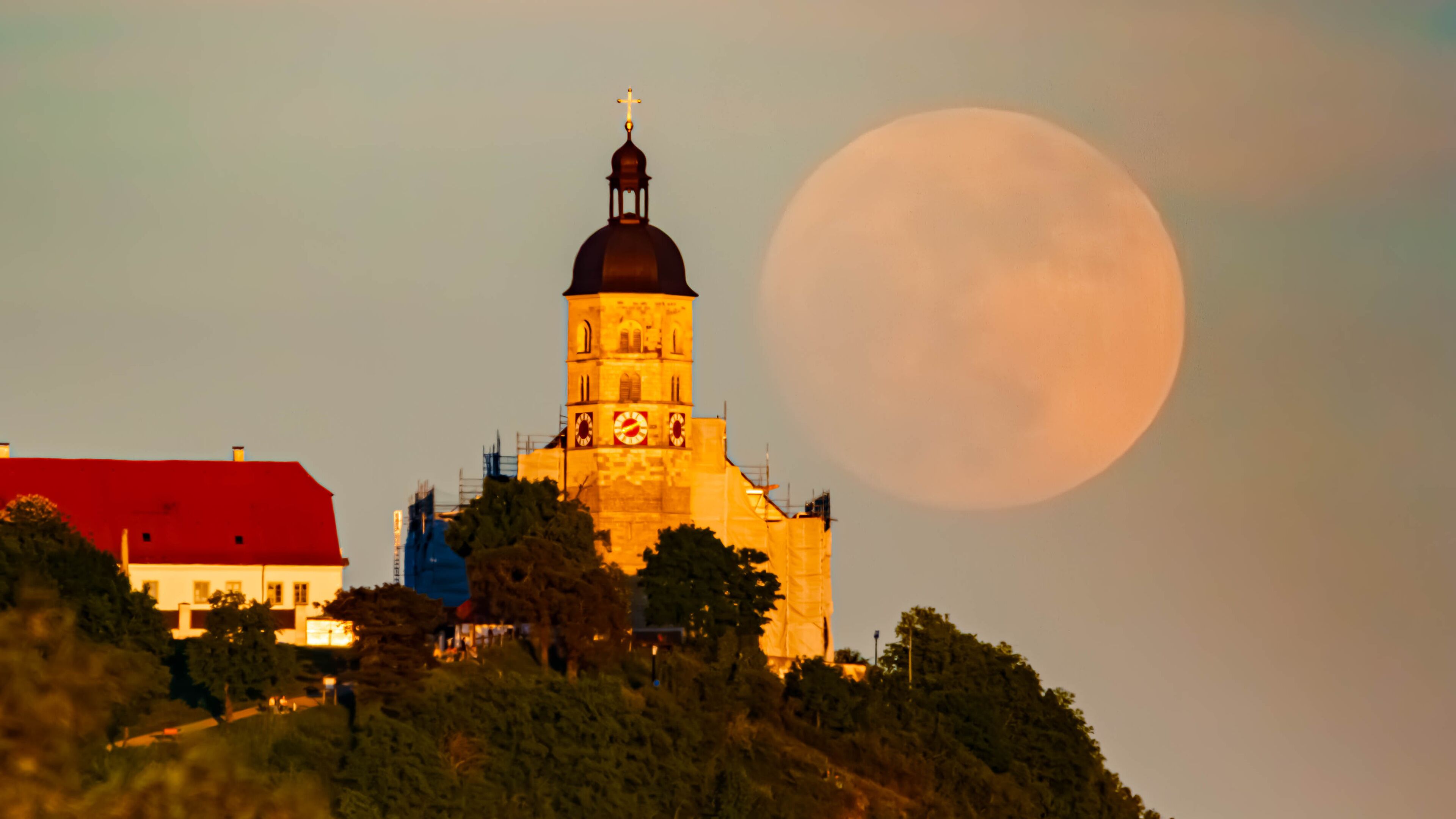 A church with a clock tower and a large moon in the sky.